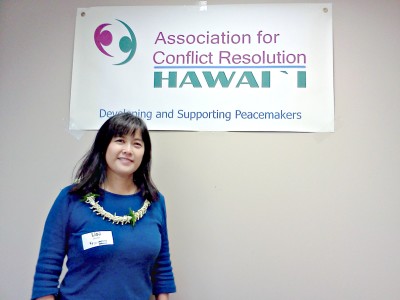 Lisa Jacobs in front of the Association for Conflict Resolution Hawaii banner